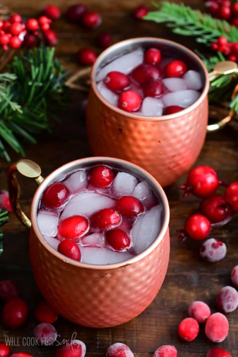 Two cranberry Moscow Mules with fresh cranberries and ice in a copper mug.