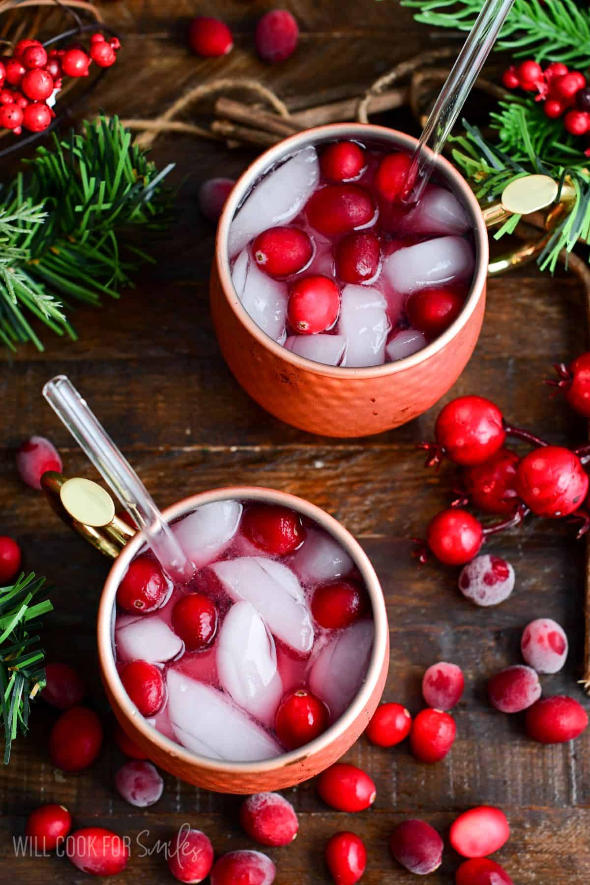 Two copper mugs filled with cranberry Moscow Mules with fresh cranberries and ice and a straw.