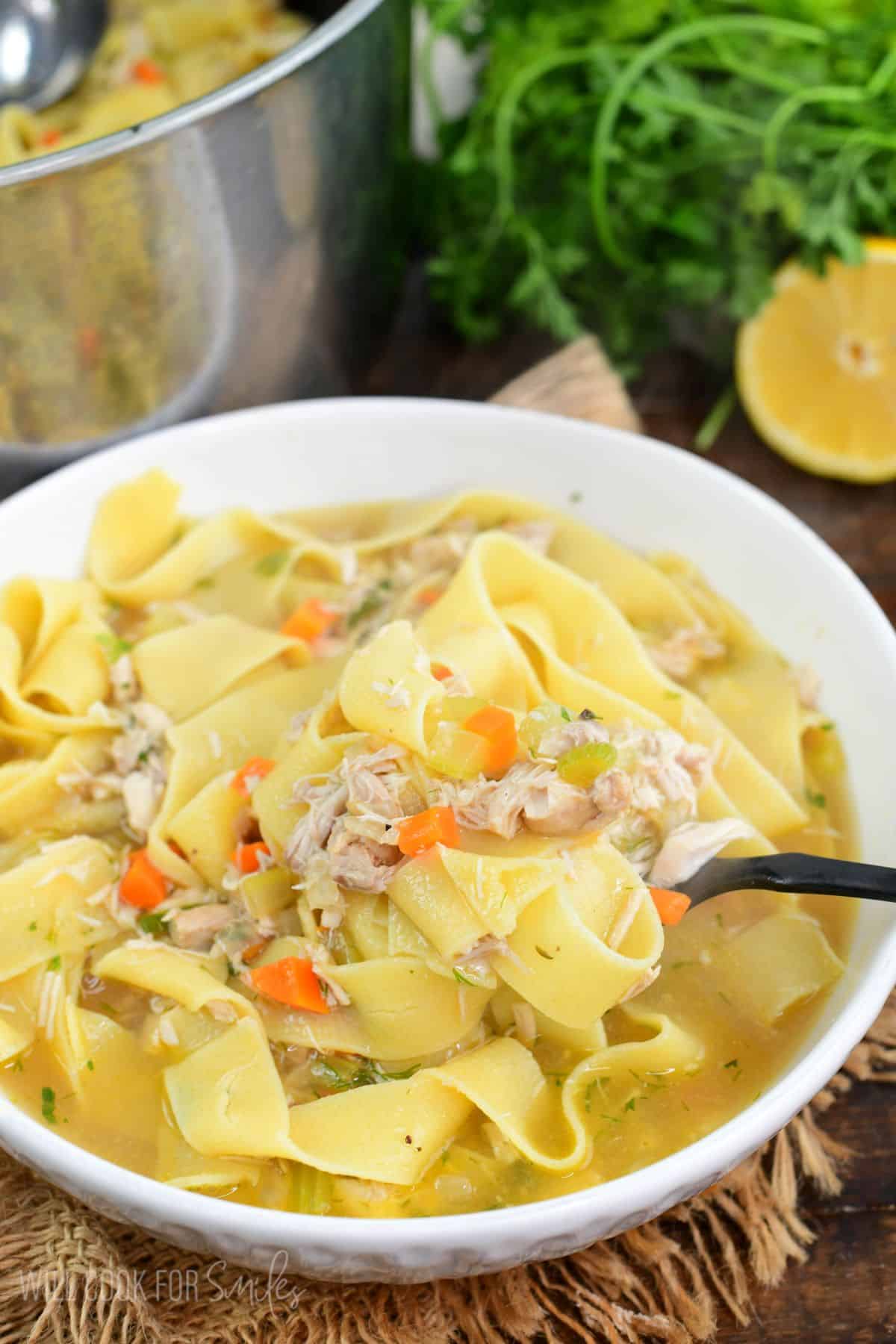 Spooning out warm homemade chicken noodle soup in a bowl with shredded chicken and vegetables.