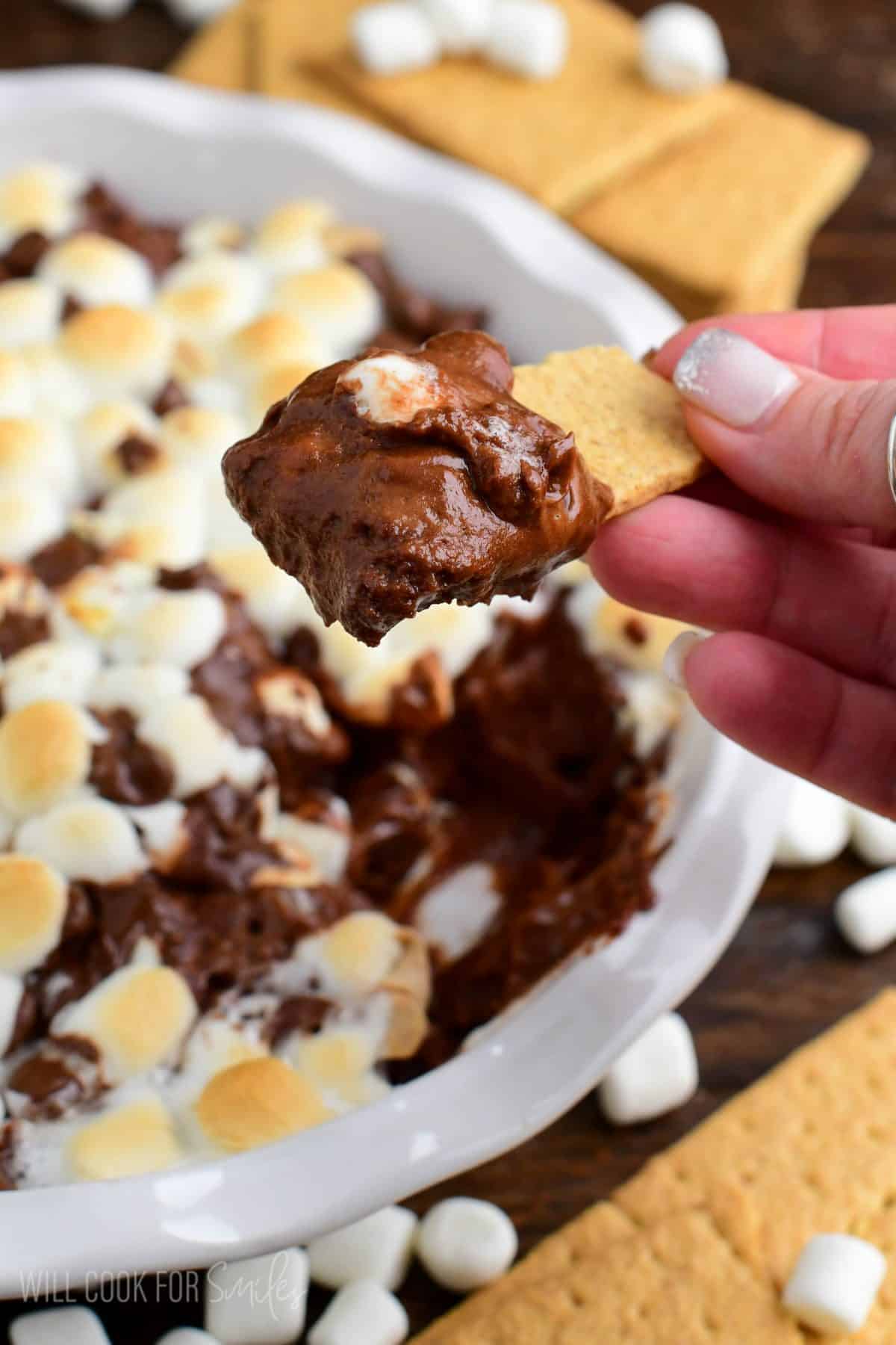holding smooth and creamy chocolate cheesecake dip on top of a graham cracker.
