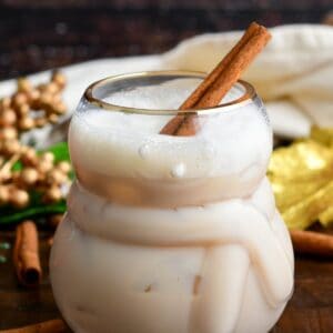 rumChata cocktail with a cinnamon sick in the glass on a wood surface.