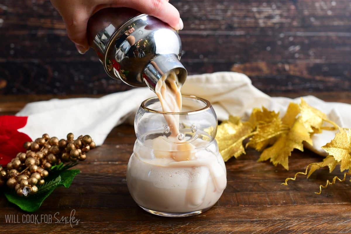 Pouring rumchata cocktail from the shaker into a snowman glass on a wood surface.