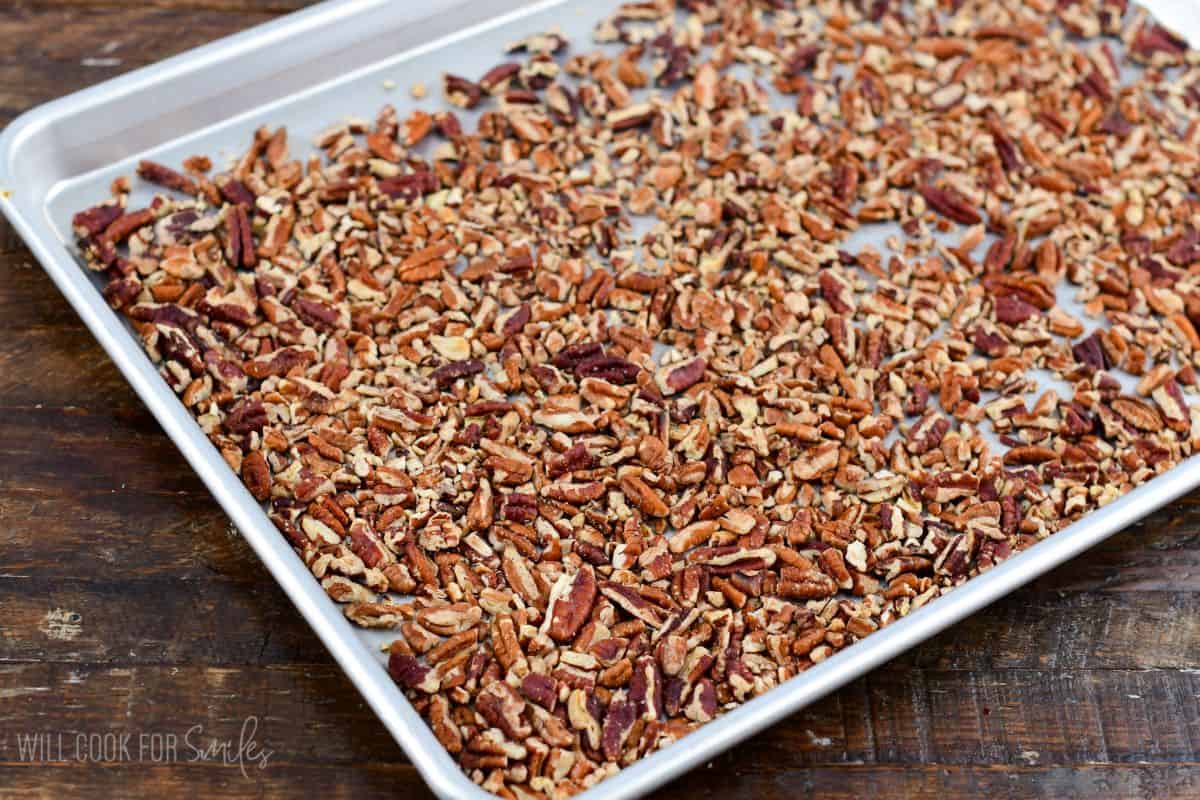 Roasted pecans on a baking sheet on a wood surface.