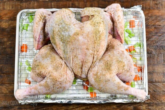 seasoned butterflied turkey on the rack of a baking sheet with veggies under.