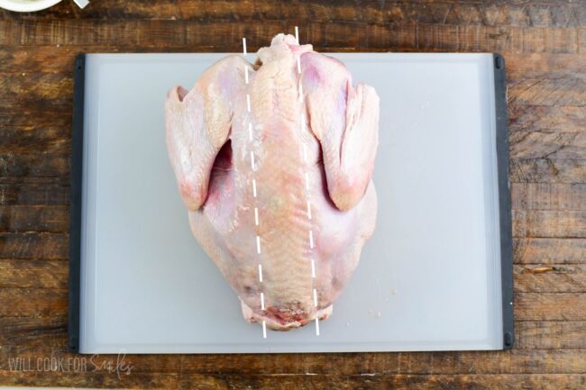 whole turkey on the cutting board with lines along where to cut to remove backbone.