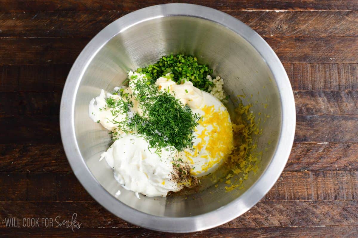 Ingredients for pickle dip in a metal bowl on a wood surface.