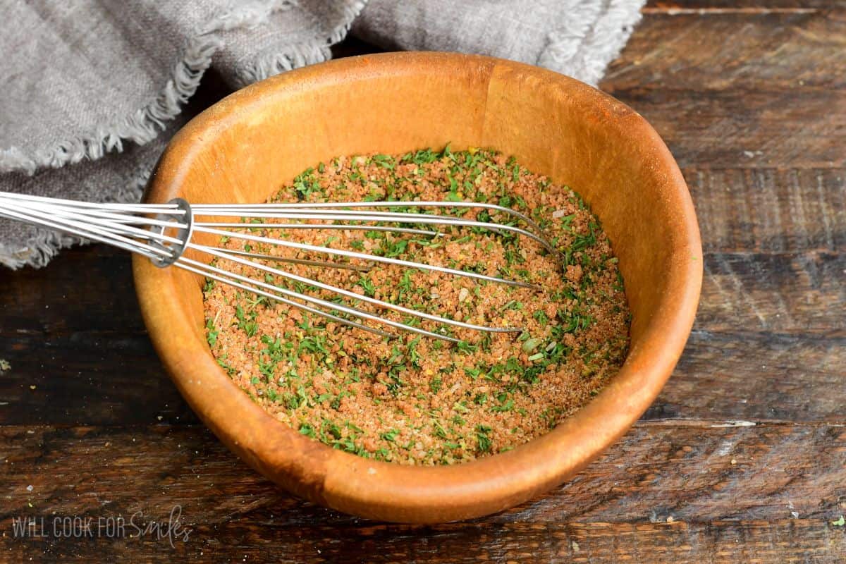 mixing pork rub with a whisk in a wooden bowl.