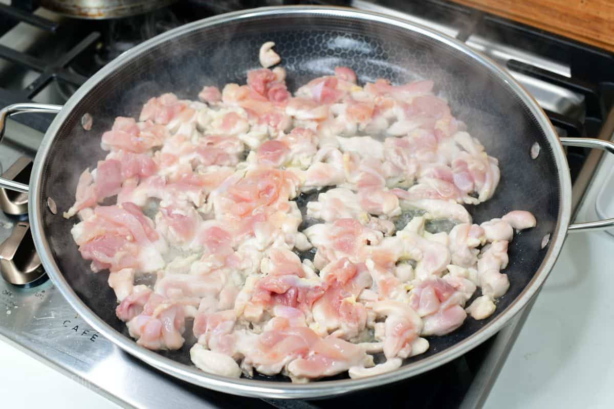 sautéing thinly sliced chicken thigh meat in a large cooking pan.