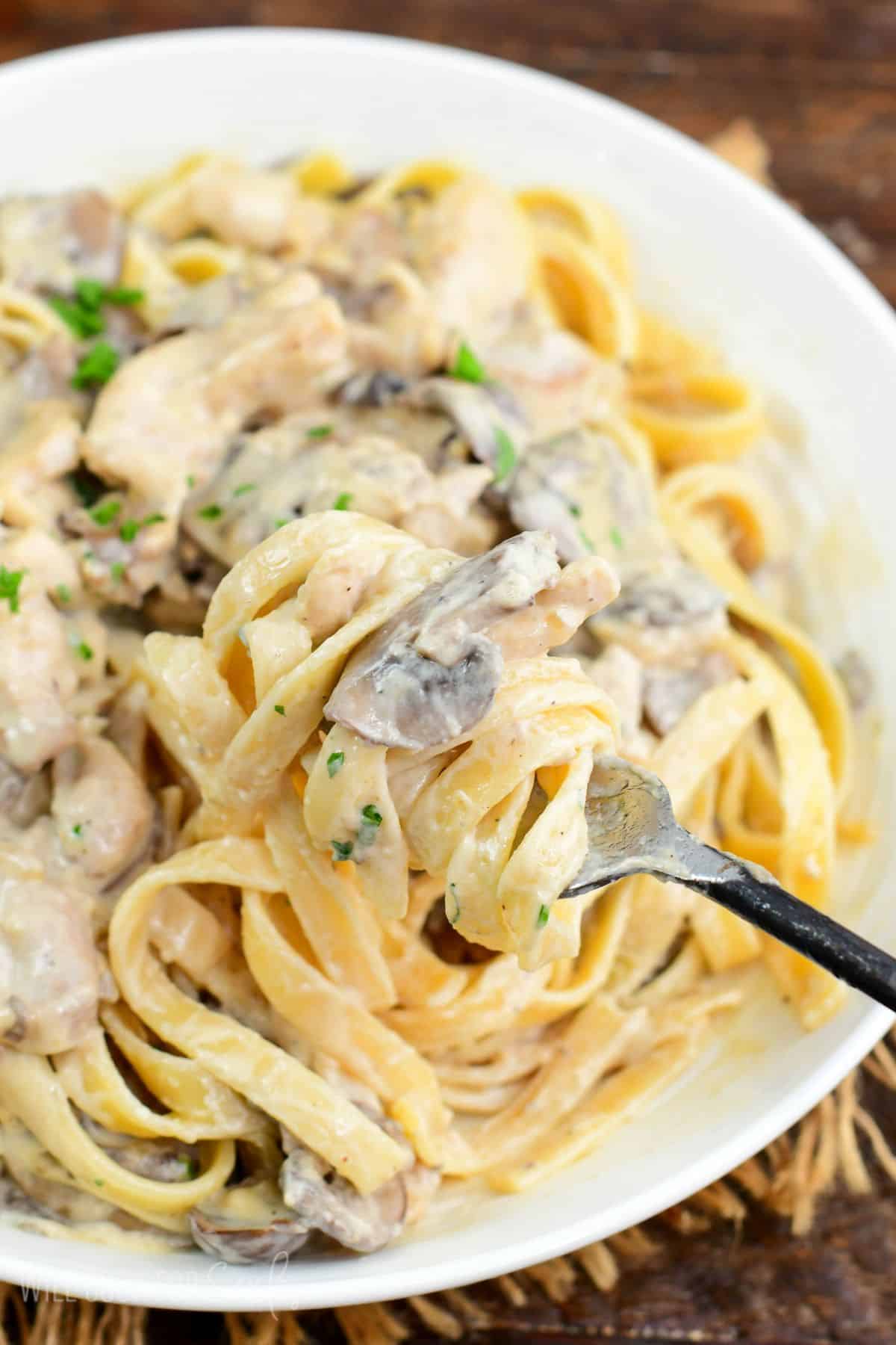 scooping some creamy pasta with chicken and mushrooms with a fork.
