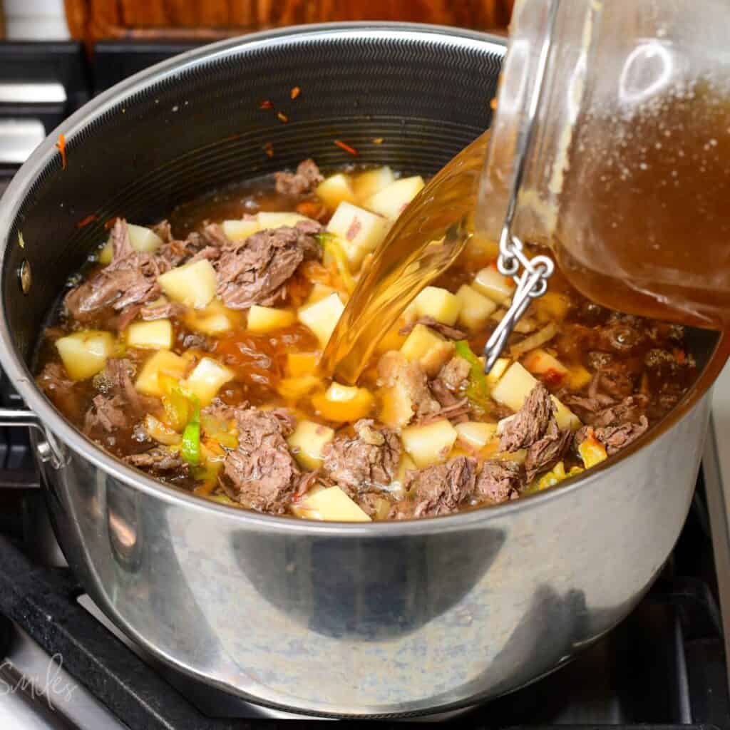 adding clear beef broth to the pot with beef, cabbage, and vegetables.