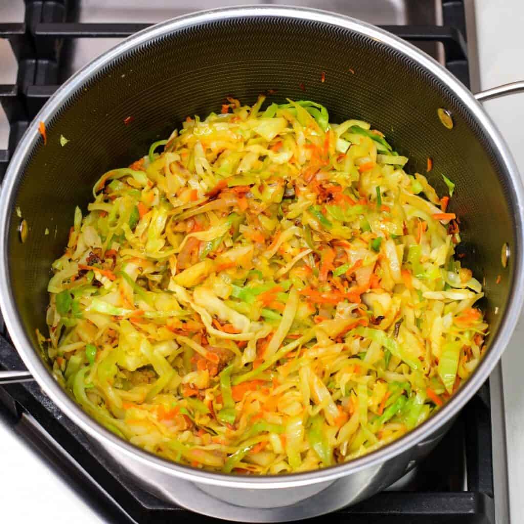 searing the finely sliced cabbage with onions and carrots in a pot.