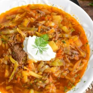 Russian beef and cabbage soup (shchi) in a white bowl with sour cream and dill and a spoon next to it.