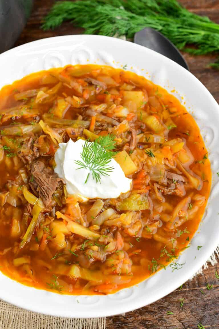 Russian beef and cabbage soup (shchi) in a white bowl with sour cream and dill and a spoon next to it.