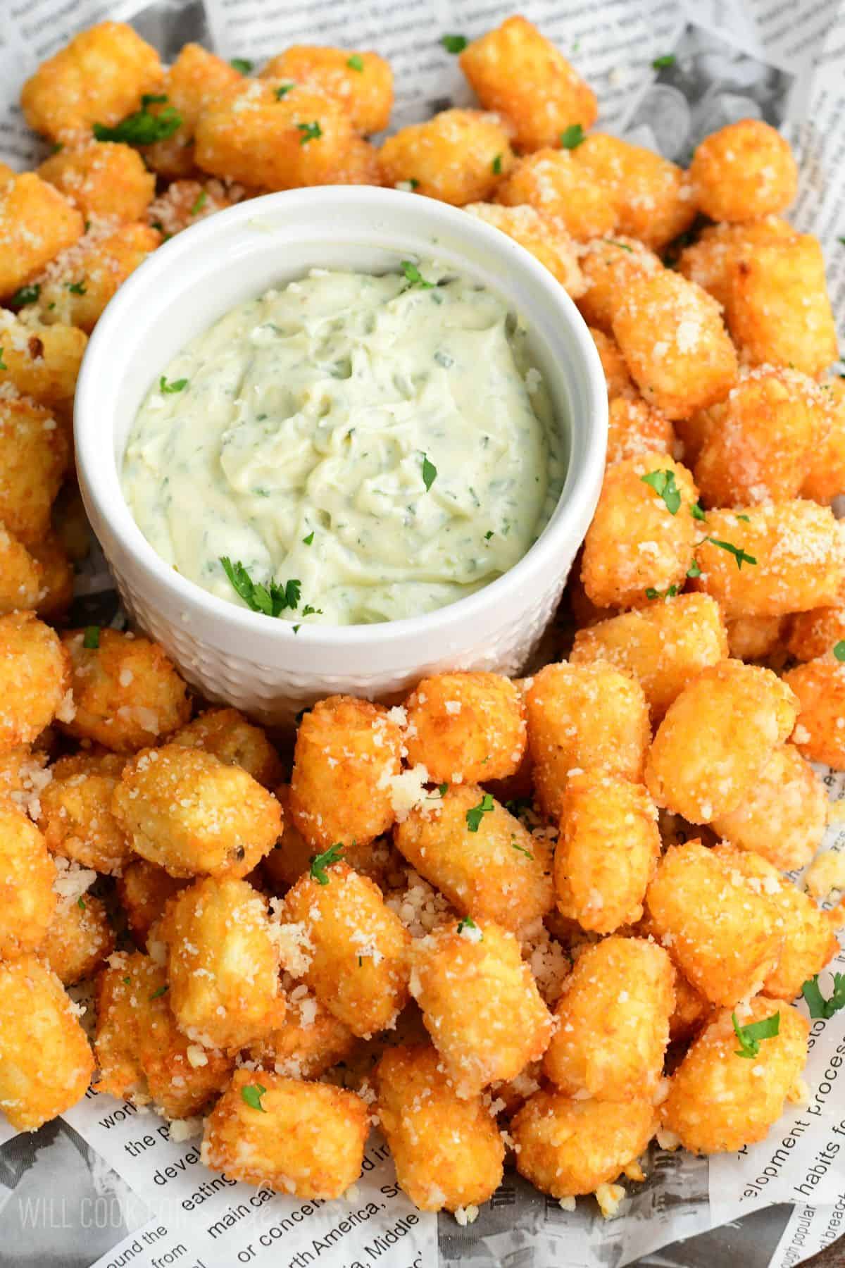Truffle tater tots on a lined tray with a garlic herb aioli in a bowl in the middle.