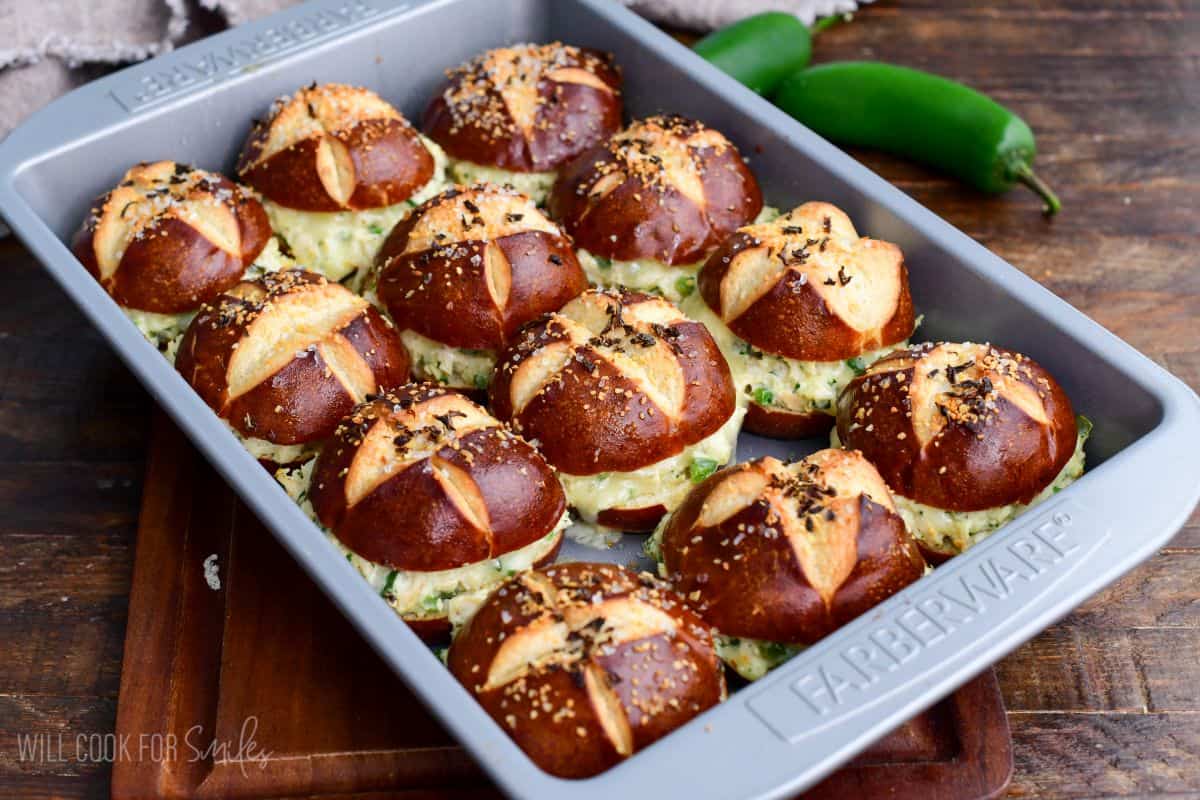 Baked jalapeño ranch chicken sliders on pretzel buns with melted cheese and creamy chicken filling served in a baking pan.