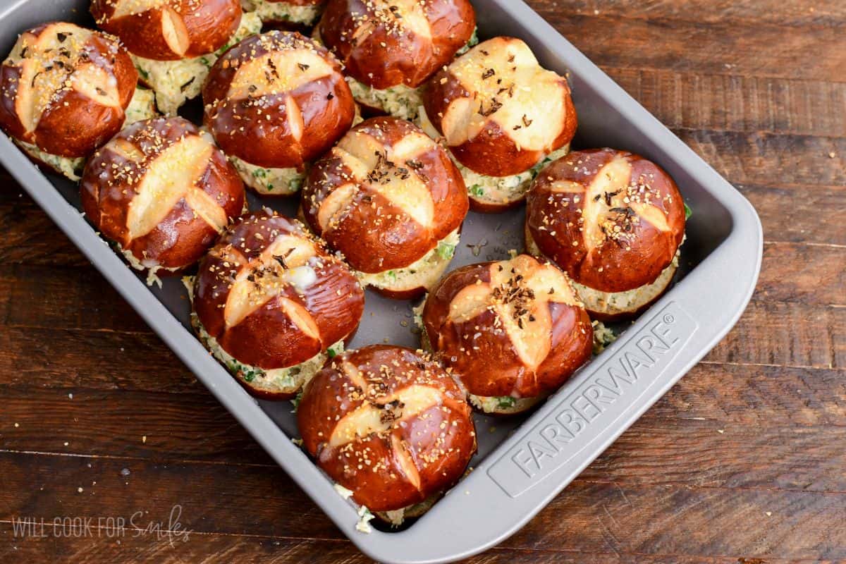 Assembled jalapeño ranch chicken sliders on pretzel buns arranged in a baking dish and seasoned before baking.