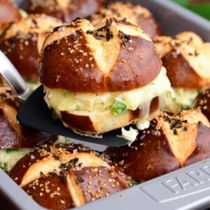 A baked jalapeño ranch chicken slider on a pretzel bun being lifted from the pan, showing melted cheese and creamy chicken filling.