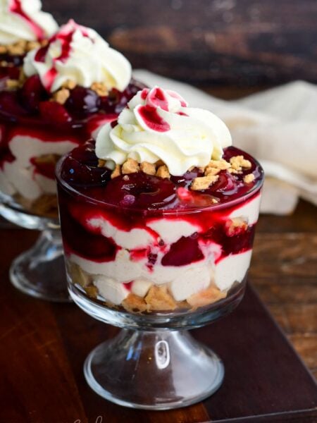 No-bake cherry cheesecake parfait layered with creamy cheesecake filling, crushed cookies, cherry topping, and whipped cream in a glass dessert cup.