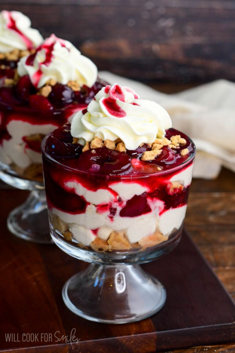 No-bake cherry cheesecake parfait layered with creamy cheesecake filling, crushed cookies, cherry topping, and whipped cream in a glass dessert cup.
