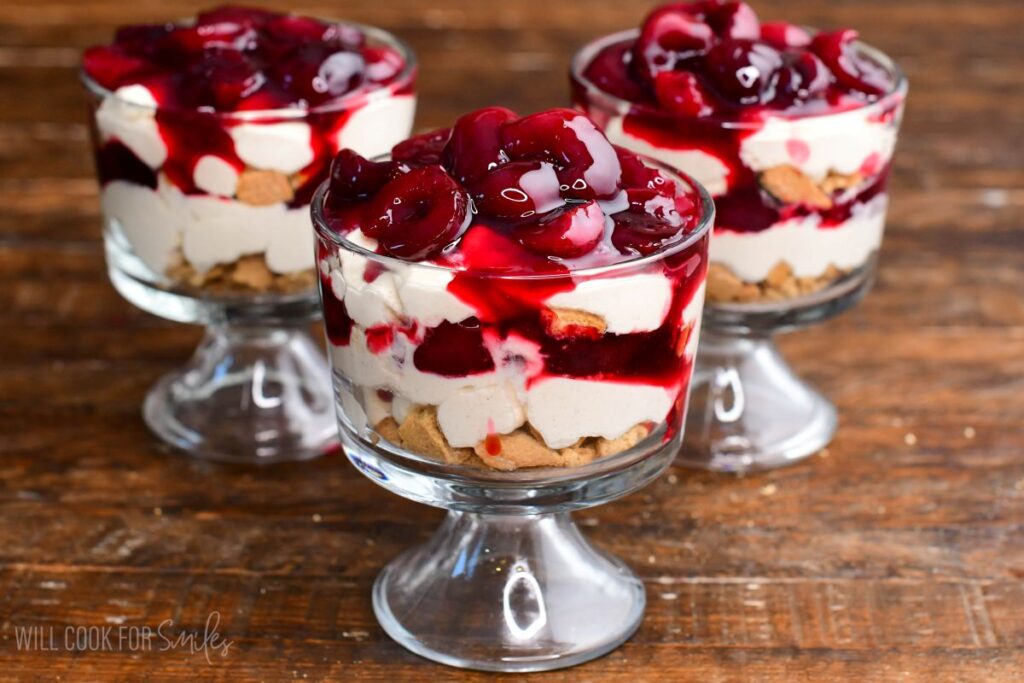 No-bake cherry cheesecake parfaits layered with crushed cookies, creamy cheesecake filling, and cherry topping in glass dessert cups.
