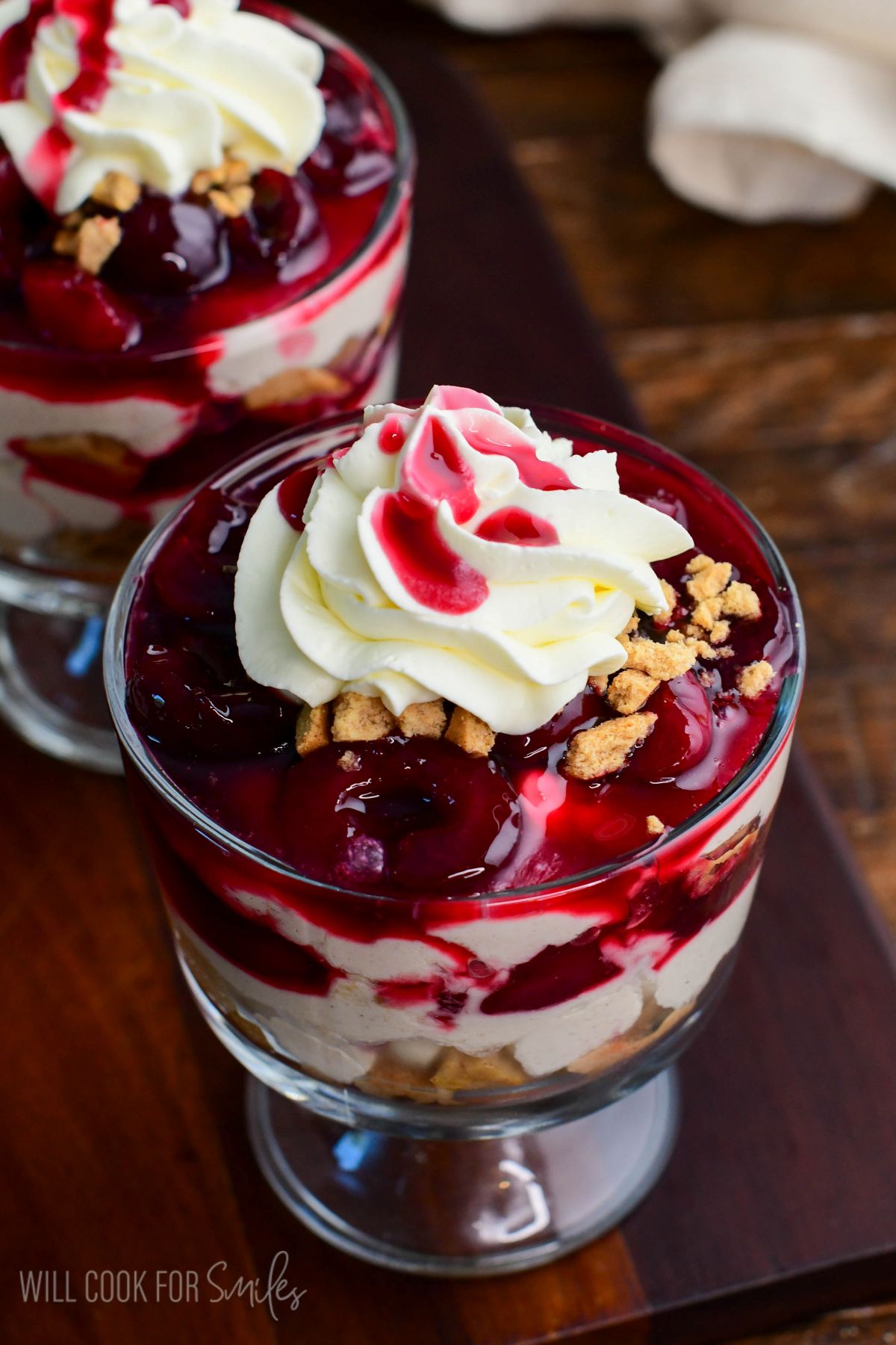 No-bake cherry cheesecake parfait topped with whipped cream, cherry sauce, and cookie crumbles in a glass dessert cup.