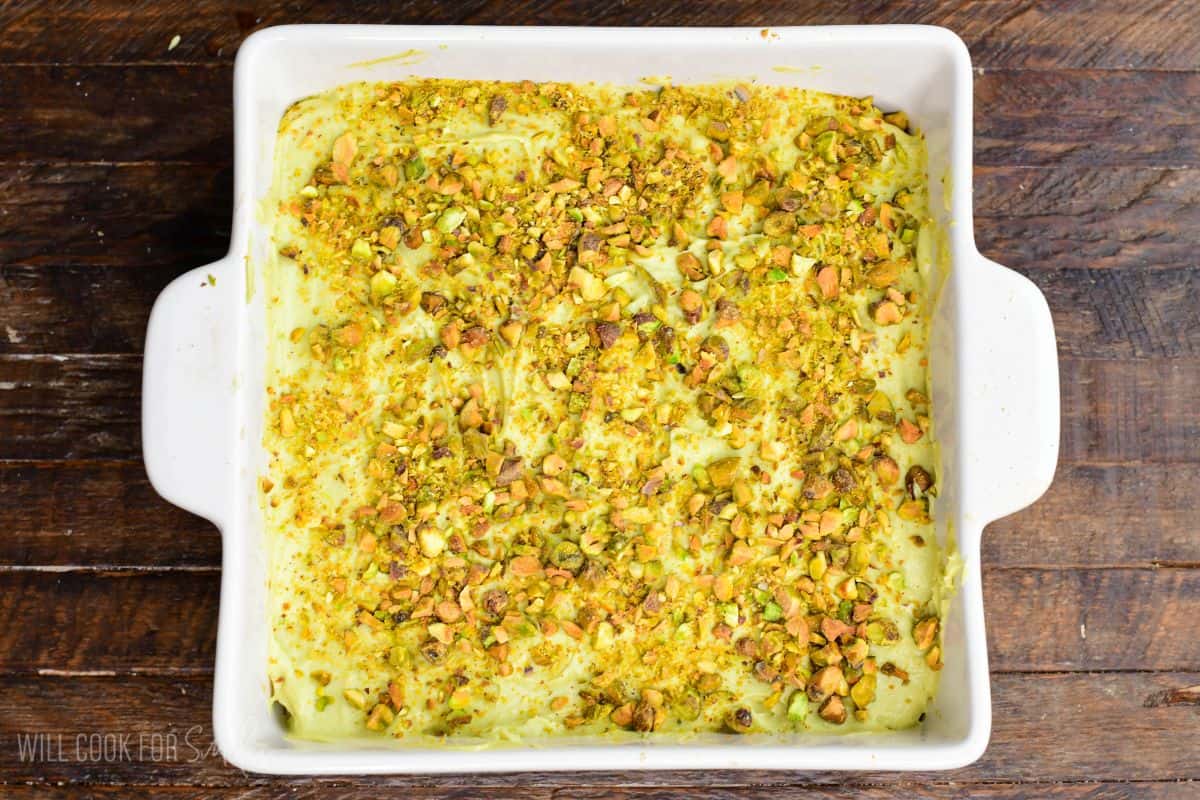 Pistachio tiramisu in a white baking dish topped with a creamy layer and sprinkled generously with chopped pistachios.