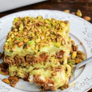 Fork with a bite of creamy pistachio tiramisu, showcasing luscious layers of pistachio mascarpone filling and coffee-soaked ladyfingers, finished with a crunchy sprinkle of chopped pistachios.