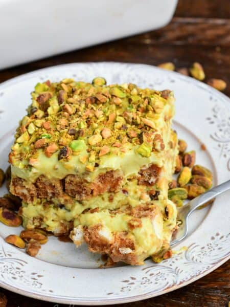 Fork with a bite of creamy pistachio tiramisu, showcasing luscious layers of pistachio mascarpone filling and coffee-soaked ladyfingers, finished with a crunchy sprinkle of chopped pistachios.