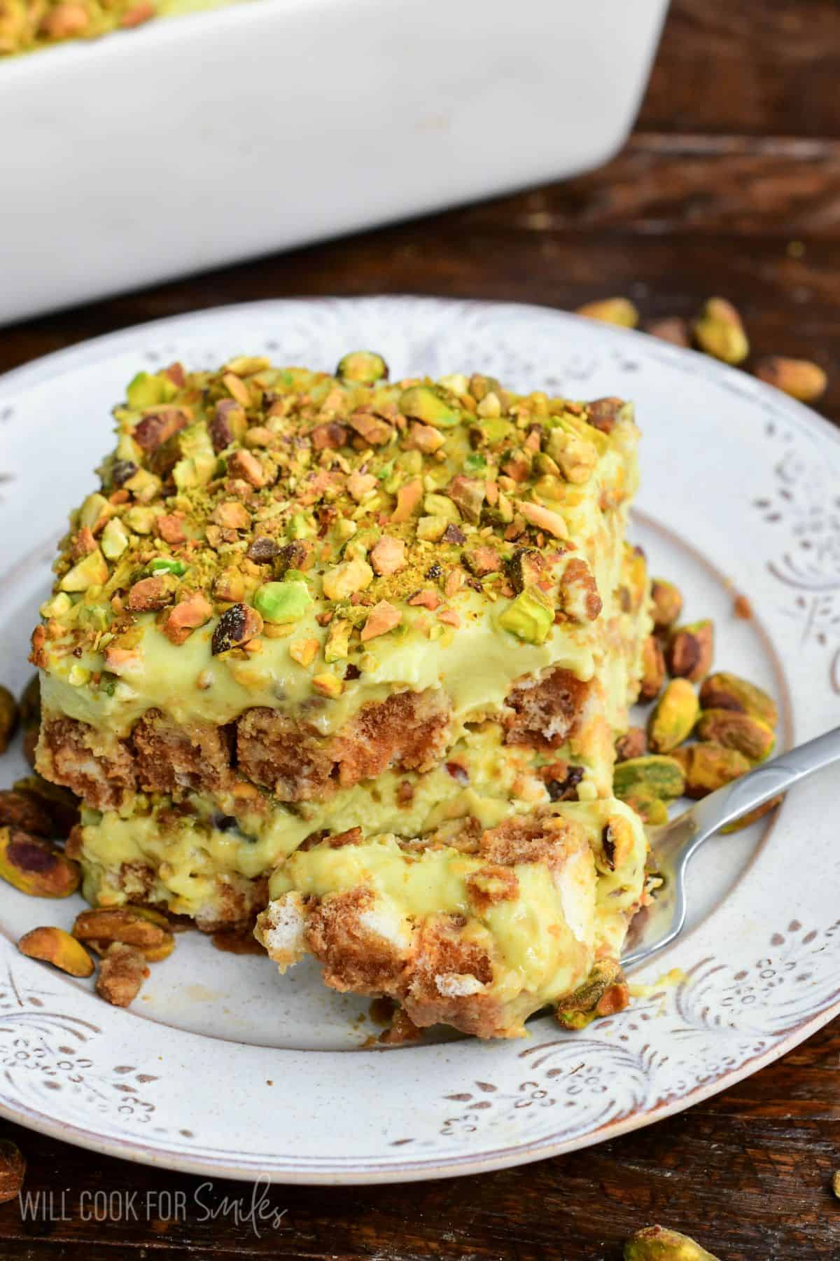 Fork with a bite of creamy pistachio tiramisu, showcasing luscious layers of pistachio mascarpone filling and coffee-soaked ladyfingers, finished with a crunchy sprinkle of chopped pistachios.