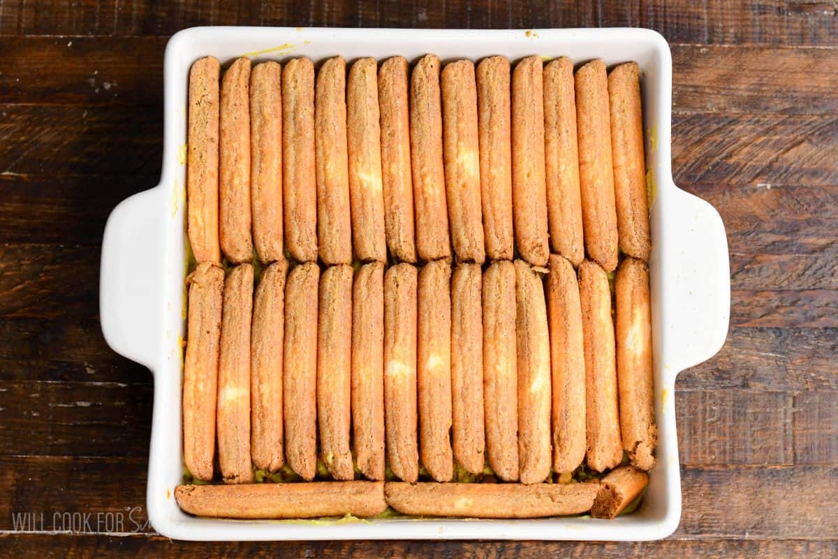 Second layer of ladyfingers neatly arranged in a white baking dish for pistachio tiramisu assembly.