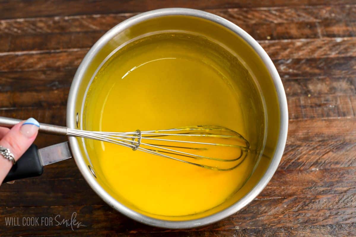Tempered egg yolk mixture being whisked in a small saucepan, creating a smooth yellow custard base.