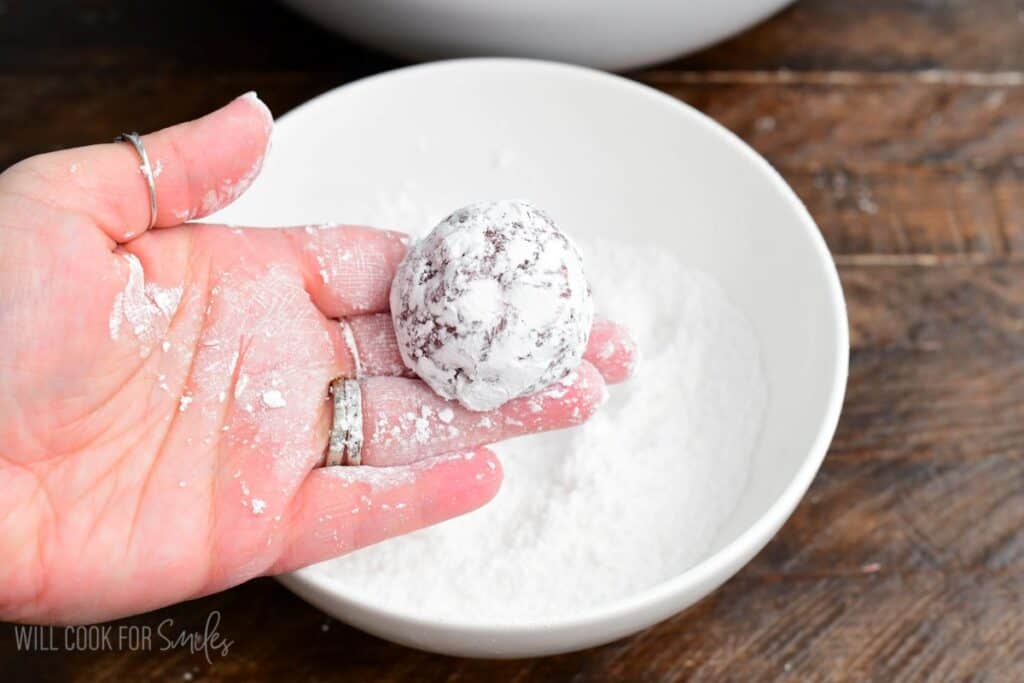 holding red velvet cream cheese cookie dough ball rolled in powdered sugar before baking.