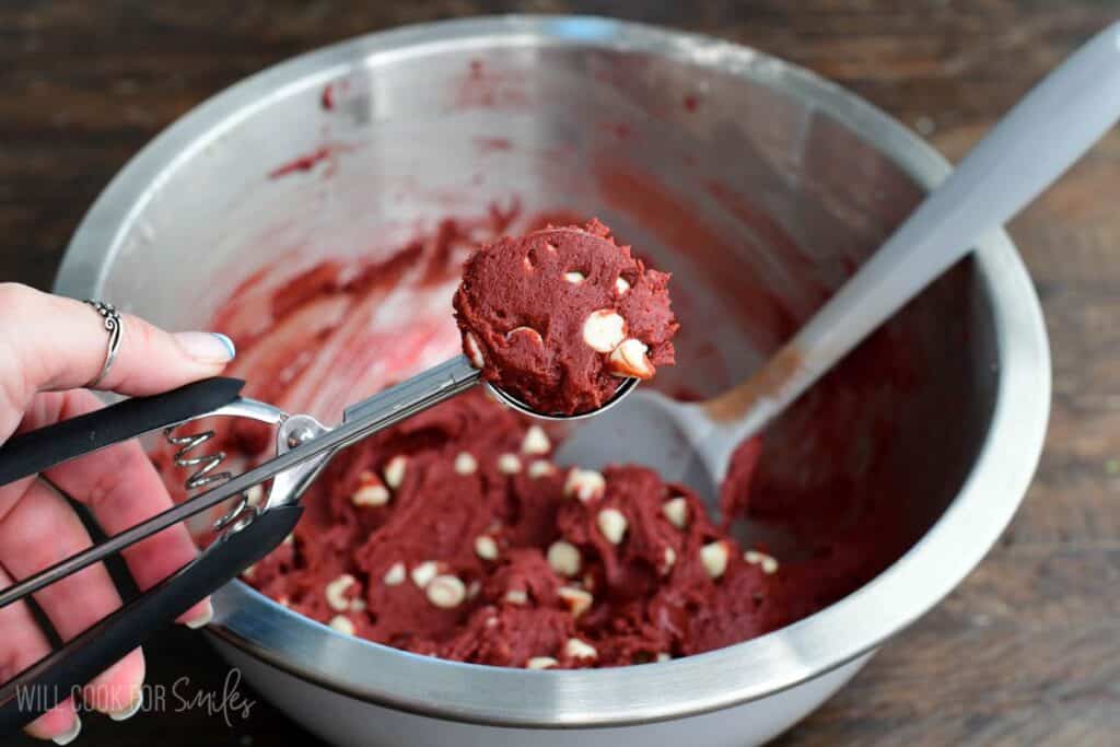 Scooping red velvet cream cheese cookie dough with white chocolate chips using a cookie scoop.