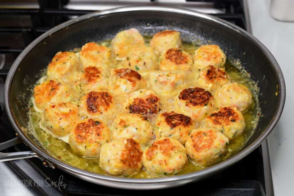 cooking the shrimp meatballs in sauce in a cooking pan on a stove.
