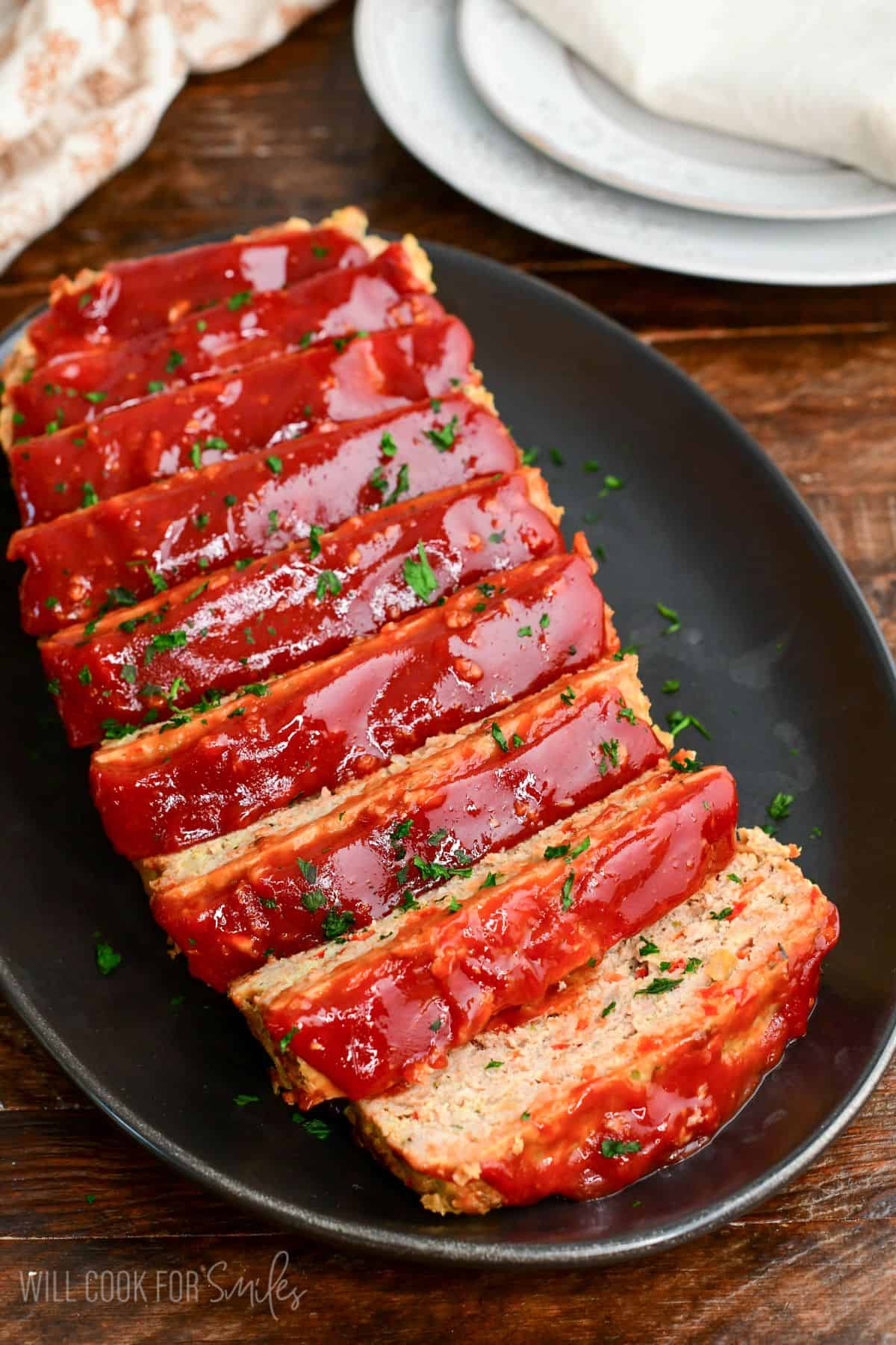 sliced juicy turkey meatloaf with ketchup topping stacked on a black platter. 
